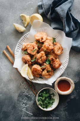 Fried shrimp served in plate with parchment paper with chopped cilantro and sauce on the side
