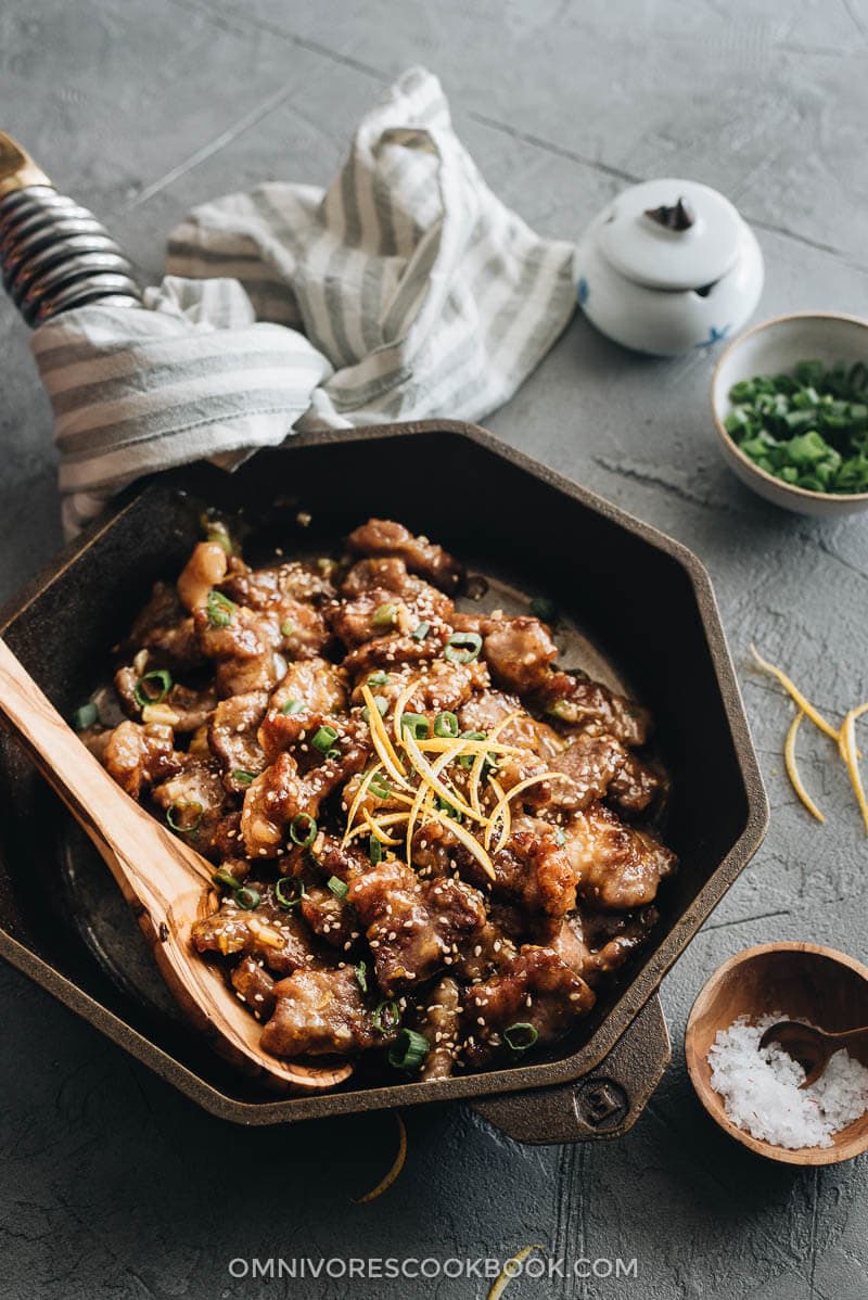 Orange beef in a cast iron skillet with orange slices garnish